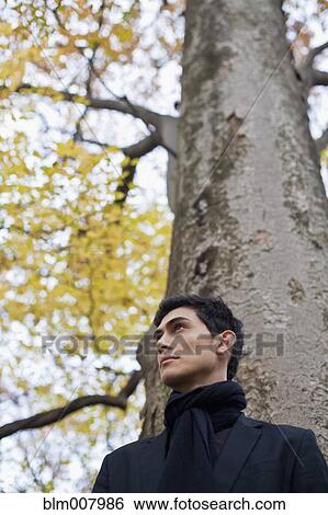 Stock Photograph - Pensive mixed race man standing under autumn tree. Fotosearch