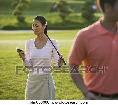 Stock Image - Pilipino golfer text messaging on cell phone. Fotosearch