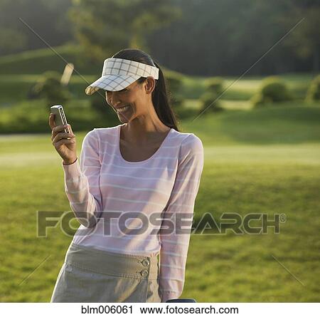 Stock Image - Pilipino golfer text messaging on cell phone. Fotosearch