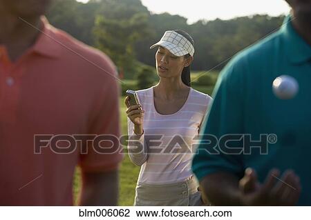 Stock Image - Pilipino golfer text messaging on cell phone. Fotosearch