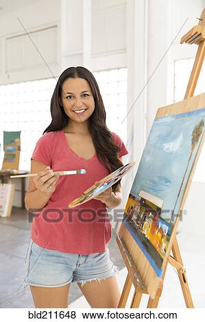 Stock Photo - Portrait of smiling woman painting at easel. Fotosearch
