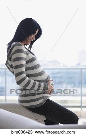 Stock Image - Pregnant Asian woman holding stomach. Fotosearch