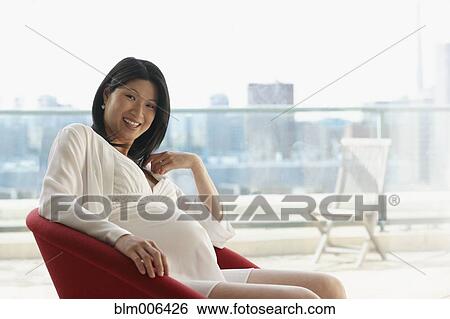 Stock Photograph - Pregnant Asian woman sitting in chair. Fotosearch