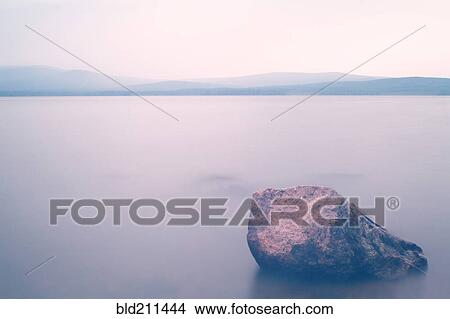 Picture - Rock on shore of serene lake. Fotosearch
