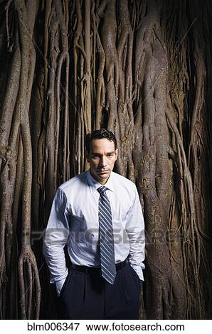 Stock Photo - Sad Latin businessman standing near tree roots. Fotosearch