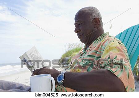 Stock Photography - Senior African man reading newspaper at beach. Fotosearch