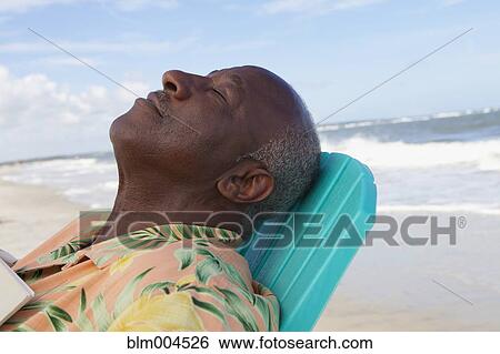 Stock Photograph - Senior African relaxing on beach. Fotosearch