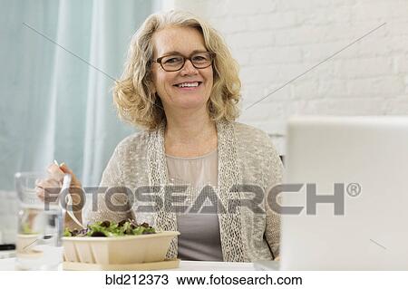 Stock Image - Senior Caucasian businesswoman eating salad. Fotosearch