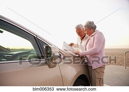 Stock Image - Senior Caucasian couple at beach looking at map. Fotosearch