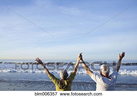 Stock Photo - Senior Caucasian couple cheering on beach. Fotosearch