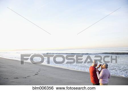 Senior Caucasian couple taking photographs on beach View Large Photo Image Stock Photograph - Senior Caucasian couple taking photographs on beach. Fotosearch