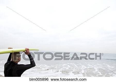 Stock Photograph - Senior Hispanic man carrying surfboard. Fotosearch