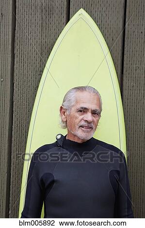 Stock Image - Senior Hispanic man with surfboard. Fotosearch