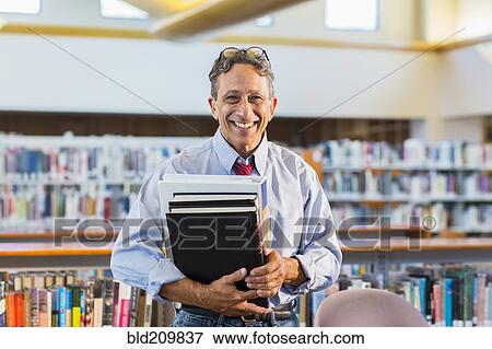 Stock Photo - Senior man holding books in library. Fotosearch