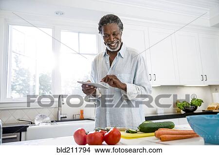 Picture - Senior man using digital tablet in kitchen. Fotosearch