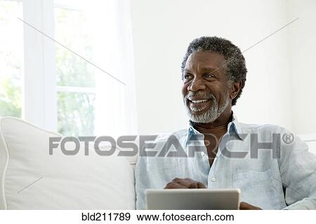 Stock Photo - Senior man using digital tablet on sofa. Fotosearch