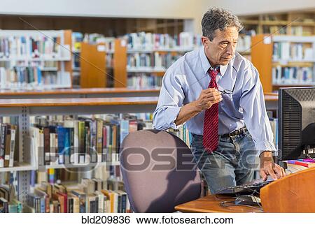 Stock Photograph - Senior man working at computer in library. Fotosearch