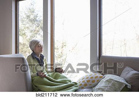 Stock Image - Senior woman meditating on sofa. Fotosearch