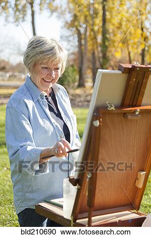 Stock Image - Senior woman painting outdoors. Fotosearch