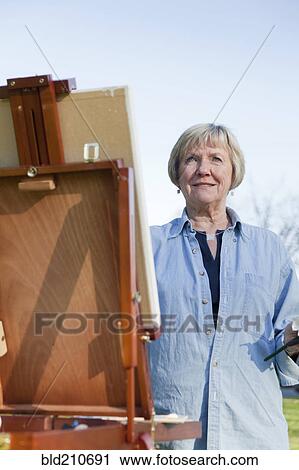 Stock Image - Senior woman painting outdoors. Fotosearch