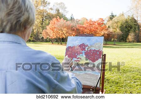 Stock Image - Senior woman painting outdoors. Fotosearch