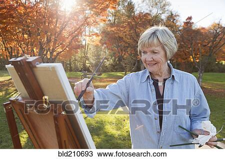 Stock Image - Senior woman painting outdoors. Fotosearch