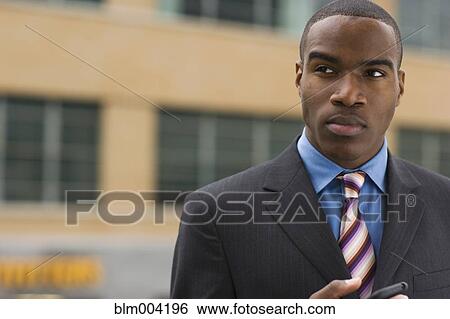Serious African businessman holding cell phone View Large Photo Image Stock Photograph - Serious African businessman holding cell phone. Fotosearch