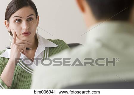 Stock Image - Serious Hispanic businesswoman listening to co-worker. Fotosearch