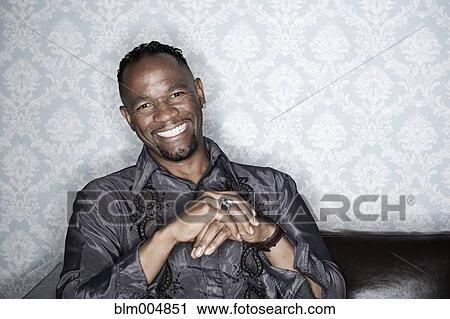 Stock Image - Serious man in elegant clothing smiling on sofa. Fotosearch