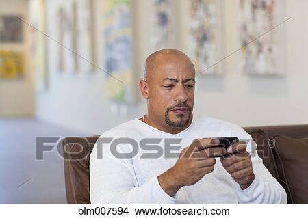 Picture - Serious mixed race man text messaging in art gallery. Fotosearch