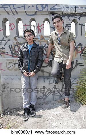 Stock Image - Serious teenage boys leaning against graffiti covered railing. Fotosearch
