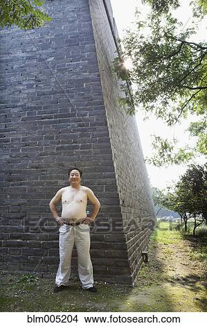 Shirtless Chinese man standing near wall View Large Photo Image Picture - Shirtless Chinese man standing near wall. Fotosearch