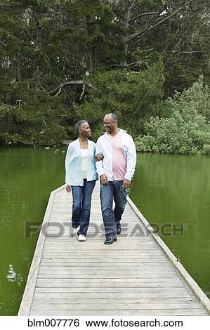 Stock Photograph - Smiling African American couple standing on pier at lake. Fotosearch