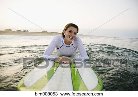 Stock Image - Smiling Caucasian teenage girl leaning on surfboard in ocean. Fotosearch
