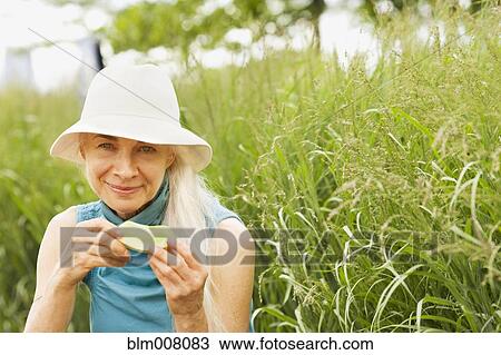 Stock Image - Smiling Caucasian woman eating in grass. Fotosearch