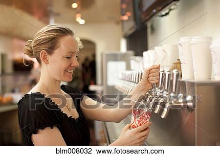 Stock Image - Smiling Caucasian woman filling cup from dispenser. Fotosearch