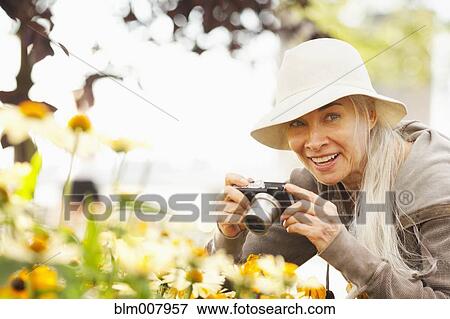 Stock Photo - Smiling Caucasian woman photographing flowers with digital camera. Fotosearch