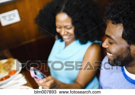 Stock Image - Smiling couple looking at cell phone in diner. Fotosearch