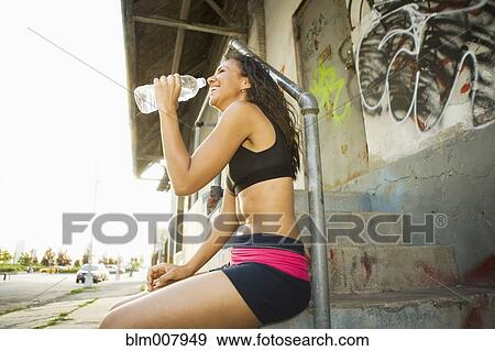 Smiling Hispanic woman drinking water on urban stairs View Large Photo Image Stock Photo - Smiling Hispanic woman drinking water on urban stairs. Fotosearch
