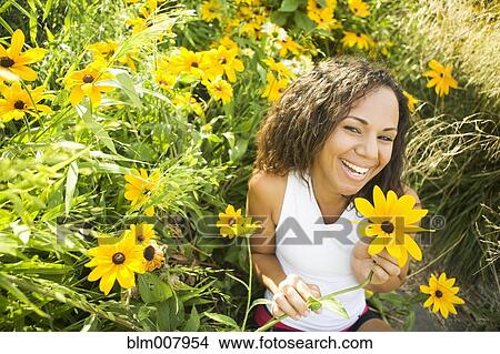 Picture - Smiling Hispanic woman sitting in field of flowers. Fotosearch