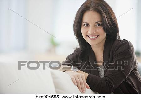 Stock Photography - Smiling Hispanic woman sitting on sofa. Fotosearch