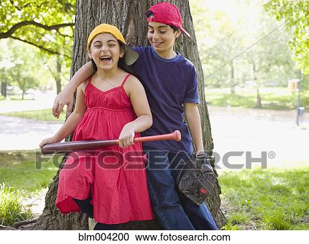 Stock Image - Smiling mixed race brother and sister holding baseball bat and mitt. Fotosearch