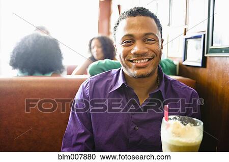 Stock Image - Smiling mixed race man with milkshake in diner booth. Fotosearch