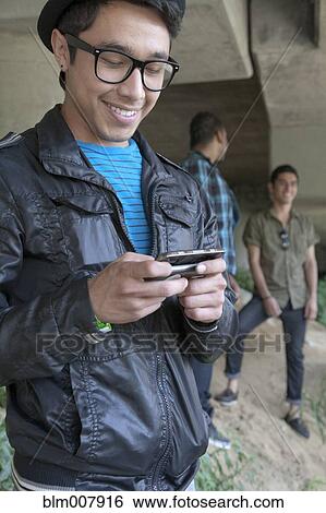 Stock Photograph - Smiling mixed race teenage boy text messaging with cell phone. Fotosearch