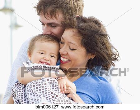 Stock Photo - Smiling parents holding daughter. Fotosearch