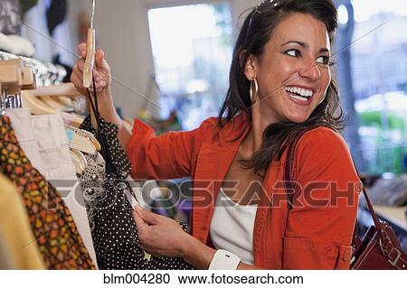 Stock Image - Smiling woman looking at price tag in clothing store. Fotosearch