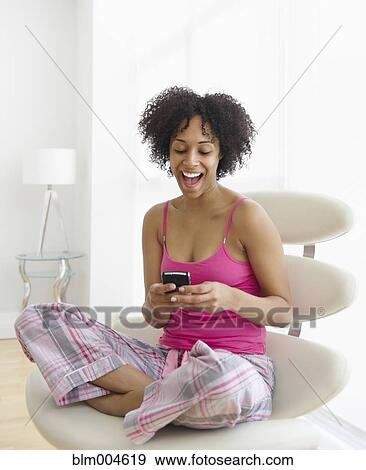 Stock Photo - Surprised mixed race woman text messaging with cell phone. Fotosearch