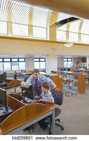 Stock Image - Teacher and student working at computer in library. Fotosearch