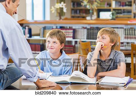 Stock Image - Teacher and students working in library. Fotosearch