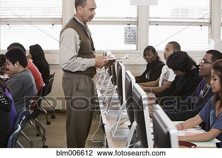 Stock Image - Teacher helping students in computer lab. Fotosearch